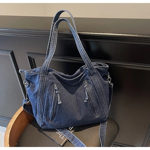 Detail of dark blue denim tote bag featuring dual front zipper pockets and top handles