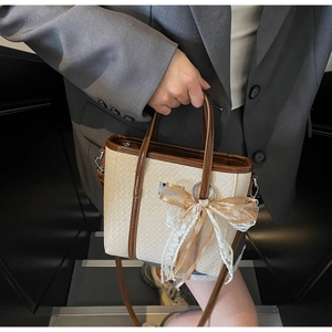 Detail of beige woven tote bag with brown leather trim and a lace bow charm accent