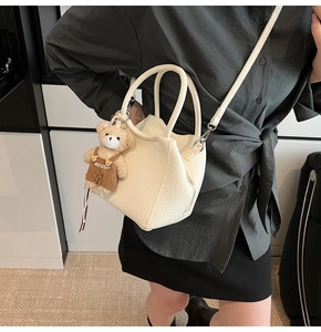 Primer plano del bolso crema con textura de lichi y colgante de osito de peluche marrón