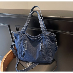 Close-up of vintage blue washed denim tote bag with diagonal zipper pockets on a leather chair