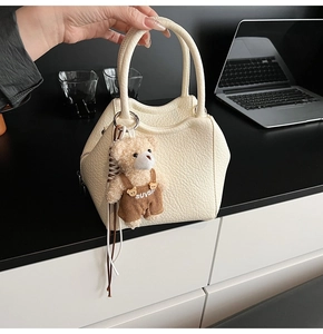 Detalle del bolso tipo cubo en cuero crema con un tierno colgante de oso de peluche