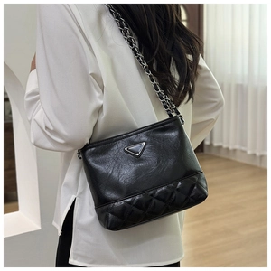 Detail of a black leather shoulder bag with quilted pattern and chain strap on a model