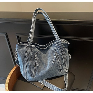 Detail of blue washed denim tote bag with dual front zipper pockets on black chair