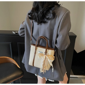 Dettaglio di una borsa tote intrecciata beige con finiture in pelle marrone e fiocco