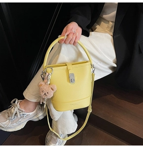Détail d'un sac seau en cuir grainé jaune vif avec boucle argentée et breloque ours en peluche
