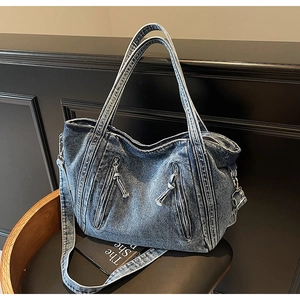 Detail of blue denim tote bag showing washed fabric texture and silver zipper pockets