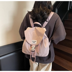 Detail of lavender canvas backpack with metal buckle and branded patch on a model