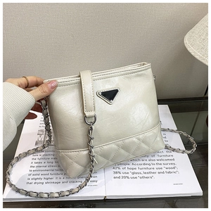 Detailed view of cream quilted bucket bag with silver chain strap and metal triangle plate