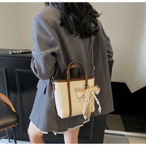 Detail of woven beige handbag with brown leather trim and decorative lace bow