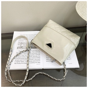 Detail shot of beige quilted bucket bag showing leather chain strap and triangle plaque