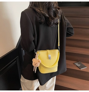 Sac seau jaune avec boucle argentée et charm ours porté sur un blazer noir élégant
