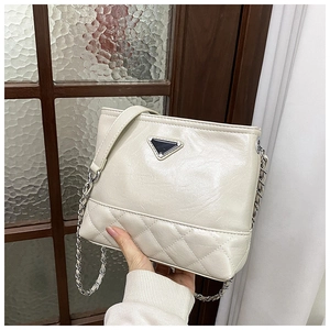 Detail showing cream quilted leather texture and triangle logo plate on shoulder bag