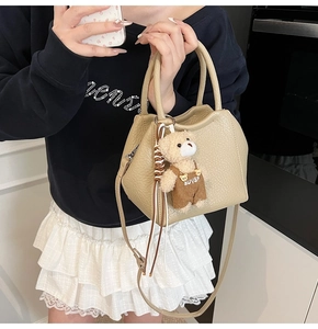 Detalle del bolso tipo cubo beige con textura de grano y colgante de osito de peluche