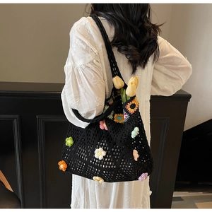 Dettaglio della borsa tote nera all'uncinetto con fiori 3D colorati indossata da modella