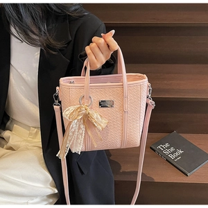 Detail view of pink woven texture bucket bag with silver logo and lace bow accessory