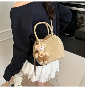 Detalle del bolso de piel con textura de lichi con oso decorativo y bandolera