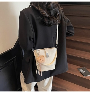 Détail du sac seau crème avec fermoir argenté et peluche ours sur un mannequin chic