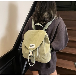 Sage green canvas backpack with metal buckle closure and side zipper pocket detail