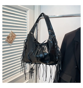 Detail of black patent leather hobo bag featuring long tassels and bow detail