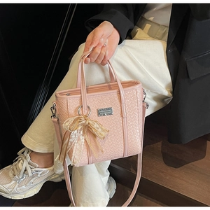Pink woven bucket bag with metallic logo and delicate lace bow charm for daily style