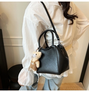 Bolso tipo cubo negro con textura de lichi y colgante de oso llevado al hombro
