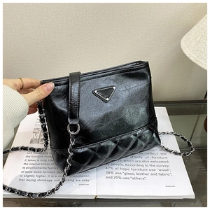Macro detail of black quilted leather texture and woven metal chain on the bucket bag