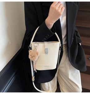 Détail d'un sac seau en cuir blanc avec fermoir argenté et charm ours en peluche