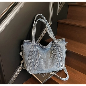 Vue détaillée d'un sac cabas en denim bleu avec fermetures éclair sur un escalier en bois
