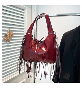 Detail of dark red faux leather tote bag with long fringe accents and glossy finish