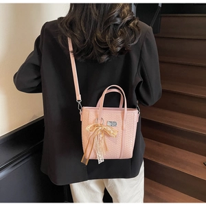 Dettaglio borsa intrecciata rosa con ciondolo a fiocco in pizzo e placca in metallo