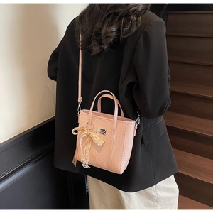Dettaglio borsa a secchiello rosa intrecciata con fiocco in pizzo e logo in metallo su pelle