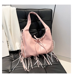 Detail of pink tassel hobo bag with glossy finish and ribbon bow on black leather chair