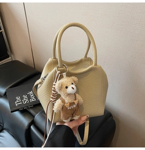 Detalle de bolso cubo amarillo con patrón de litchi y colgante de oso de peluche