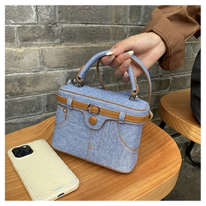 Detail of vintage blue denim box bag with brown leather trim and metal buckle accents