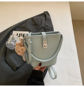 Gros plan sur le sac seau en cuir bleu clair grainé avec son charm ours en peluche