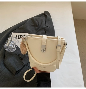 Gros plan du sac seau beige en cuir avec boucle argentée et pompon en fourrure