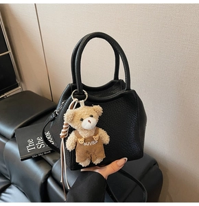 Primer plano de un bolso tipo cesta negro con detalle de dije de oso de peluche