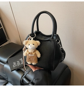 Detalle de bolso negro con textura de litchi y colgante de osito sobre asiento de piel