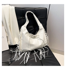 Close-up of a white hobo bag with long tassels and bow detail on a black leather sofa