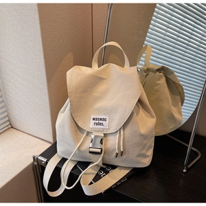 Detailed shot of beige nylon backpack featuring silver metal buckle and side drawstring design