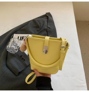 Détail du sac seau en cuir jaune avec fermoir argenté et accessoire en peluche doux