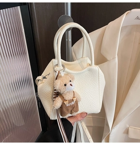 Detalle de bolso cubo blanco con textura de lichi, colgante de oso y asas de mano