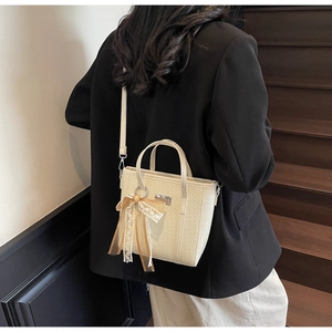 Detail of cream bucket bag with woven texture, metal plaque and decorative lace bow