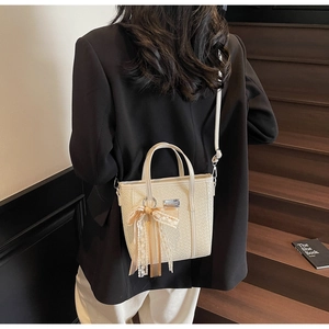 Dettaglio borsa a secchiello intrecciata off-white con fiocco in pizzo e logo argento