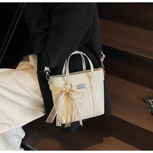 Cream white woven bucket bag detail with lace bow charm and metal logo plate shown on model