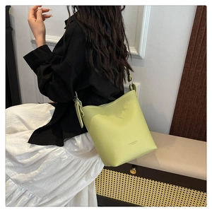 Detail of lime green bucket bag with lychee texture and wide strap on a model