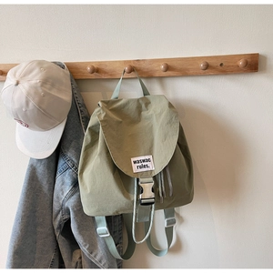 Detail of light green canvas backpack with silver buckle and woven brand label