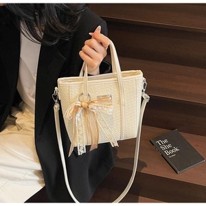 Detail of cream woven bucket bag with lace ribbon bow and metal charm on wooden stairs