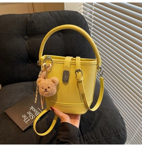 Détail du sac seau en cuir jaune à motif litchi avec boucle en métal et breloque