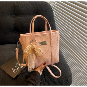 Detail of pink woven bucket bag with lace ribbon and metallic logo plate decoration